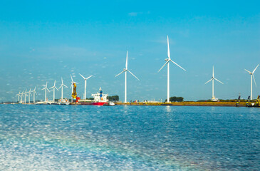 A seaport on the outskirts of Amsterdam with wind generators on the shore and solar panels mounted on quay poles, water splashes with a rainbow in the foreground.