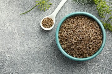 Bowl of dry seeds, spoon and fresh dill on grey table, flat lay. Space for text