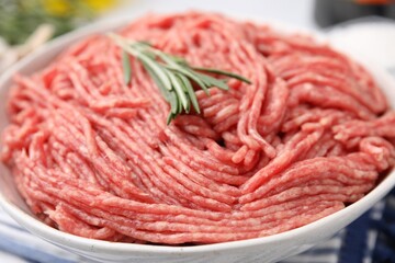 Fresh raw ground meat and rosemary in bowl on table, closeup