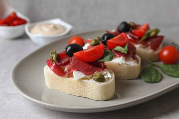 Delicious sandwiches with bresaola, cream cheese, olives and tomato on light grey table, closeup