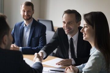 Happy businessman shake hand of new business partner, celebrate conclusion of great deal, reach agreement, sign contract, smiling team leader welcomes colleague at team brainstorming meeting at office