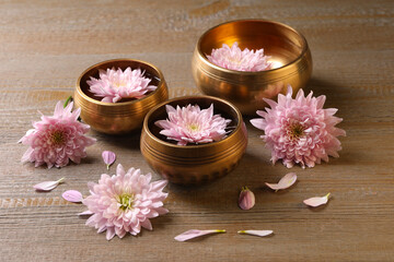 Obraz na płótnie Canvas Tibetan singing bowls with water and beautiful flowers on wooden table