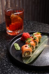 Delicious sushi rolls served with alcoholic Negroni cocktail on dark table