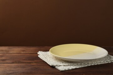 Fototapeta na wymiar Beautiful ceramic plate and napkin on wooden table against brown background, space for text
