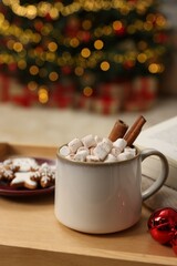 Christmas cocoa with marshmallows and cinnamon sticks in grey cup on wooden tray indoors, closeup. Space for text