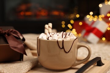 Delicious cocoa with marshmallows and chocolate topping on floor against fireplace and Christmas gifts, closeup
