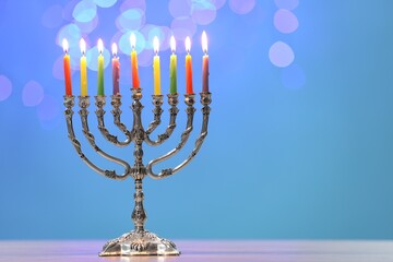 Hanukkah celebration. Menorah with burning candles on table against blurred lights, space for text