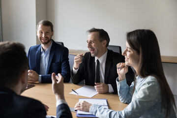 Group of businesspeople laugh at funny joke in boardroom, talk, take break at briefing, enjoy work moments with friendly colleagues, at corporate seminar. Teamwork, companionship teambuilding event