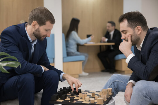 Two office employees, millennial workmate, businessmen in formal wear play chess take break during workday in modern coworking space or office cafe, develop strategic skills, training brainwork. Hobby