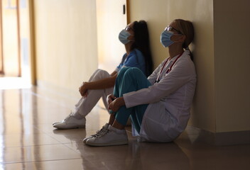 Young female doctor and nurse in medical masks sit in corridor of hospital. Emotional burnout of...