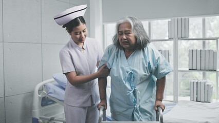 young asian nurse supports elderly Asian female patient tries to walk with walker in hospital