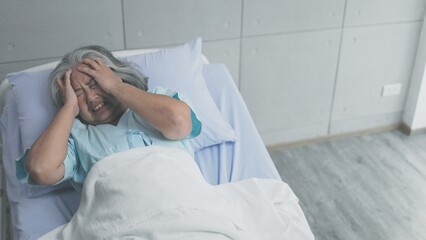 Asian elderly woman having migraine headaches on the bed in hospital 