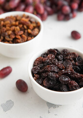 Bowls of brown and dark raisins with ripe red grapes on light background.Macro.