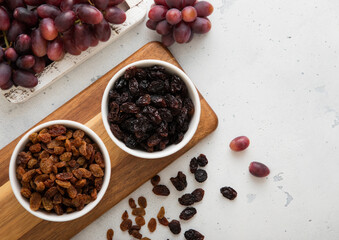 Two bowls with dried raisins with ripe red grapes on light background.Top view.