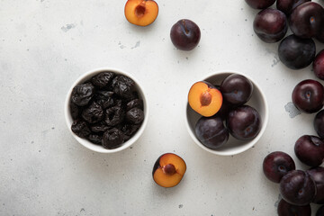 Two bowls with dried prunes and ripe raw plums on light background.Top view. - obrazy, fototapety, plakaty