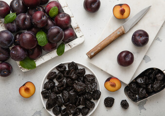 Sweet prunes on plate and scoop with ripe plums in wooden box on light kitchen background.