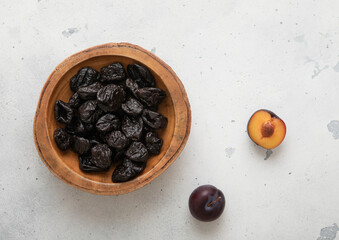 Wooden bowl with sweet dried prunes on light kitchen background.