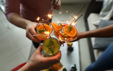 Alcoholic cocktails with fruit pieces, mint and sparklers close up top view. Three people hold...