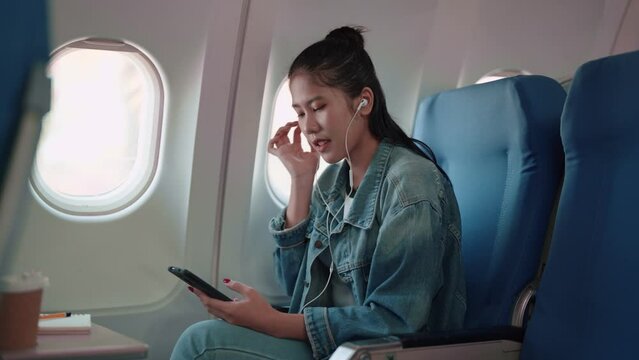Asian female traveler enjoys her journey with headphones, playing music from her smartphone. Immerse in her travel playlist, blending the beats with the excitement of a long weekend getaway