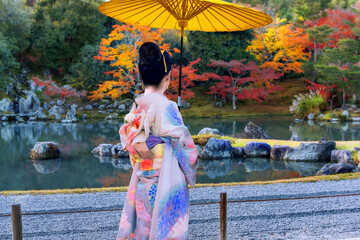 Woman in kimono with yellow umbrella in park during autumn. - 687458019