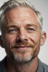 Obraz premium Close-up of a portert of a handsome gray-haired smiling man of 50-60 years old with blue eyes looking at the camera. A direct look, a smile, emotions.