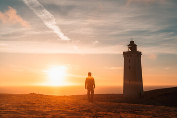 Mann steht vor verlassenem Leuchtturm am Rubjerg Knude in Dänemark während des Sonnenuntergangs.