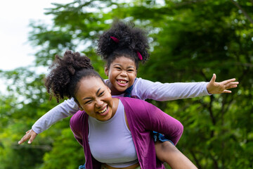 African American mother is playing piggyback riding with her young daughter while having a summer...