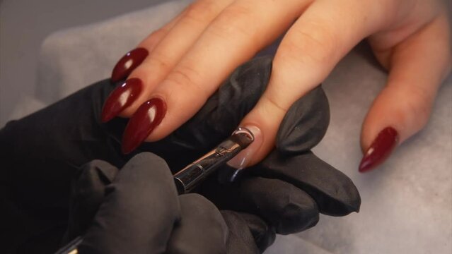 Manicurist in black gloves is painting a finger nail with a special gel