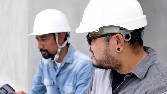 Closeup Asian two engineering male wearing hardhat using smartphone contact customer or inspector sitting in construction site, worker, architect, manager, business partner working with Indian labor