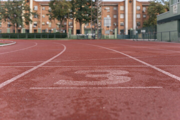 Lane number 3 of the athletics track. Image of the reddish rubber of the high performance sports track of a local city.