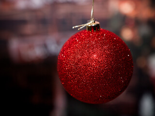 A big shinny red Christmas ball hanging on a golden string against a blurred moody background. Holiday season background with empty space for text