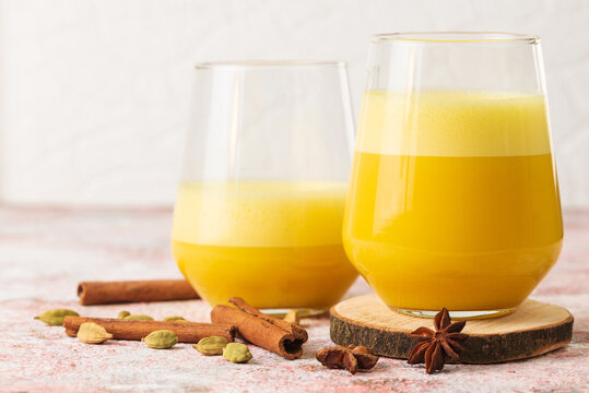 Two portions turmeric latte or warm milk drink with spices cardamom, cinnamon stiks in glasses on the table