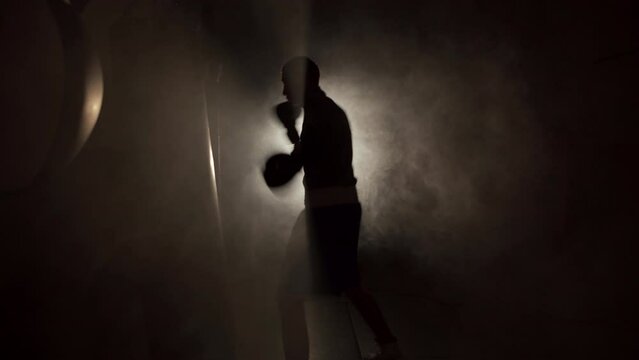 Male boxer impacting on punching bag over black smoke background. Boxer training hard.