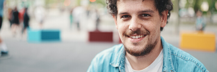  closeup portrait of young bearded man in denim shirt posing and smiling at camera on modern...