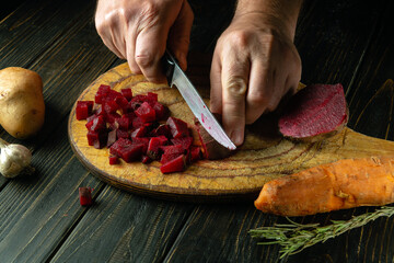 Cutting boiled beets into small pieces with a knife to prepare a vinaigrette. Knife in the hand of...