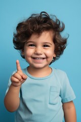 Delighted toddler giving a peace sign, against a serene blue studio background