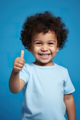Happy toddler giving a thumbs up, on a vibrant blue studio backdrop