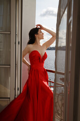 Fototapeta na wymiar Beautiful slender brunette in a long red dress on the balcony.