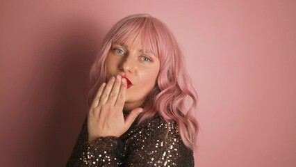 Beautiful pink hair woman with makeup blows kiss, demonstrates her good feelings, says goodbye on distance, isolated over pink background. Young pretty female model makes air kiss. High quality FullHD