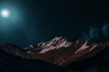 Night view of snowy mountain peaks in the light of moon and stars - 687494243