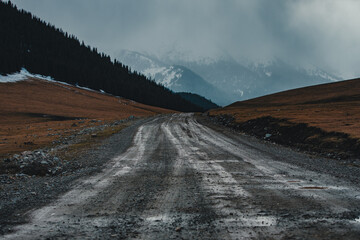 Mountain landscape with muddy dirt road in cloudy cold weather