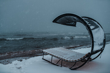 Sun lounger on the beach during snowstorm in cold winter