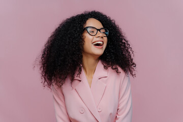 Joyful woman with curly hair laughing in a stylish pink blazer