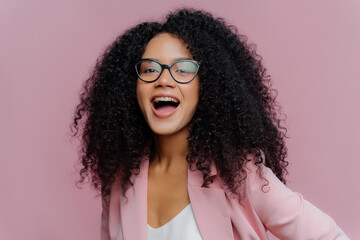 Exuberant young woman in glasses and pink blazer laughing joyfully.