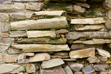 Old rough stone wall made of various square natural stones in beige, gray and brown colors.