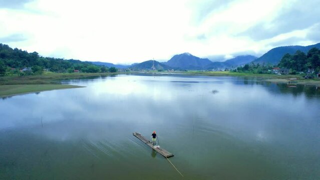 Establish aerial view of fishermen fishing using traditional bamboo rafts in a beautiful swamp surrounded by mountains in Agam Regency, West Sumatra.