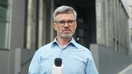 Handsome Caucasian correspondent talking about interesting announcement on camera while holding microphone. Successful reporter telling news while standing in middle of street. TV journalism.