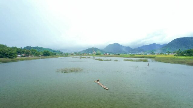 Establish aerial view of fishermen fishing using traditional bamboo rafts in a beautiful swamp surrounded by mountains in Agam Regency, West Sumatra.