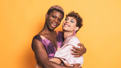 Stylish trans men in make up and fashion clothes embracing and smiling on yellow