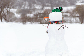 Large snowman in knitted scarf and hat side view. Winter entertainment. Christmas background.